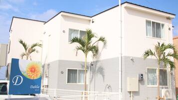 A two-story building with a white exterior, multiple windows, and a fenced outdoor area with palm trees.