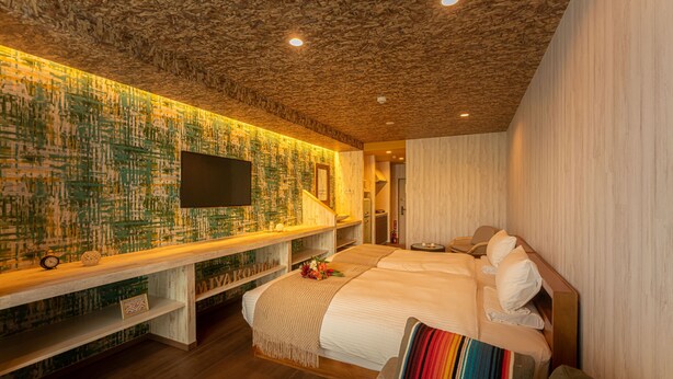 Una habitación de hotel moderna con techo de madera, una cama grande, un televisor montado en la pared y un banco de madera con una mesita.