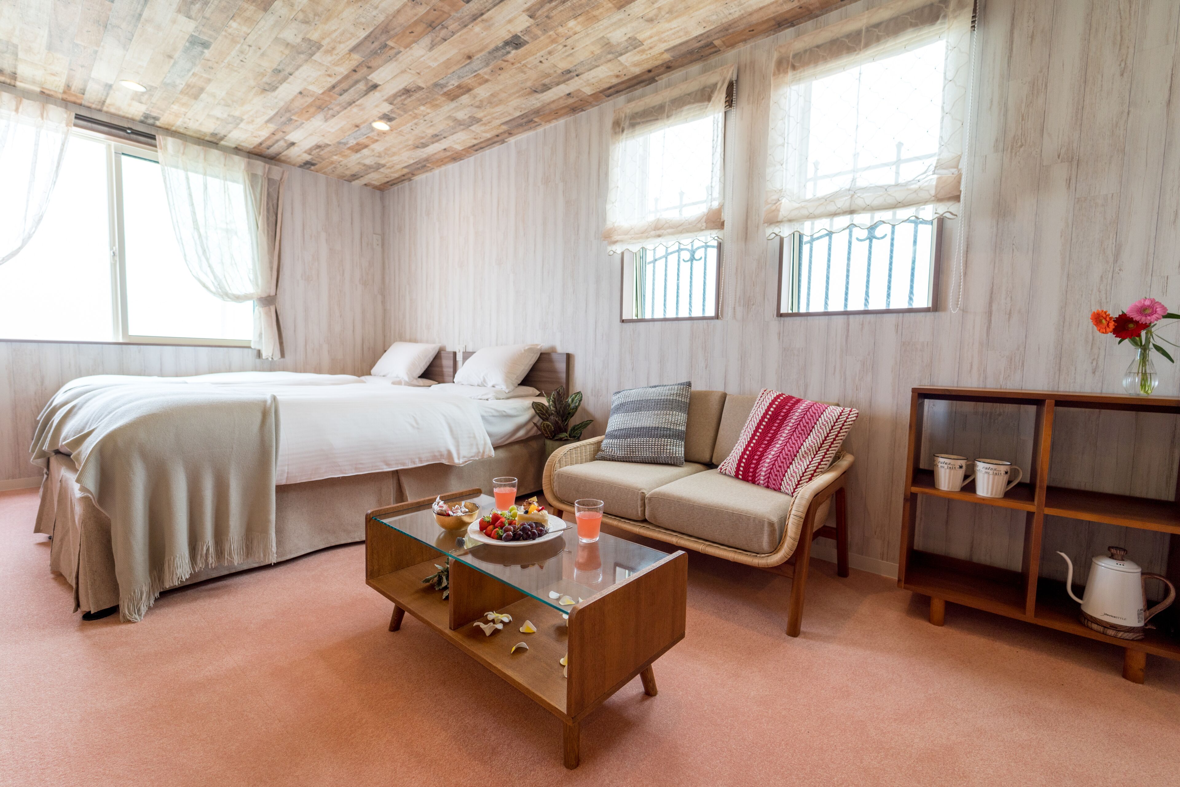 A bedroom with a bed, a sofa, a coffee table, and a shelf with cups and a teapot.