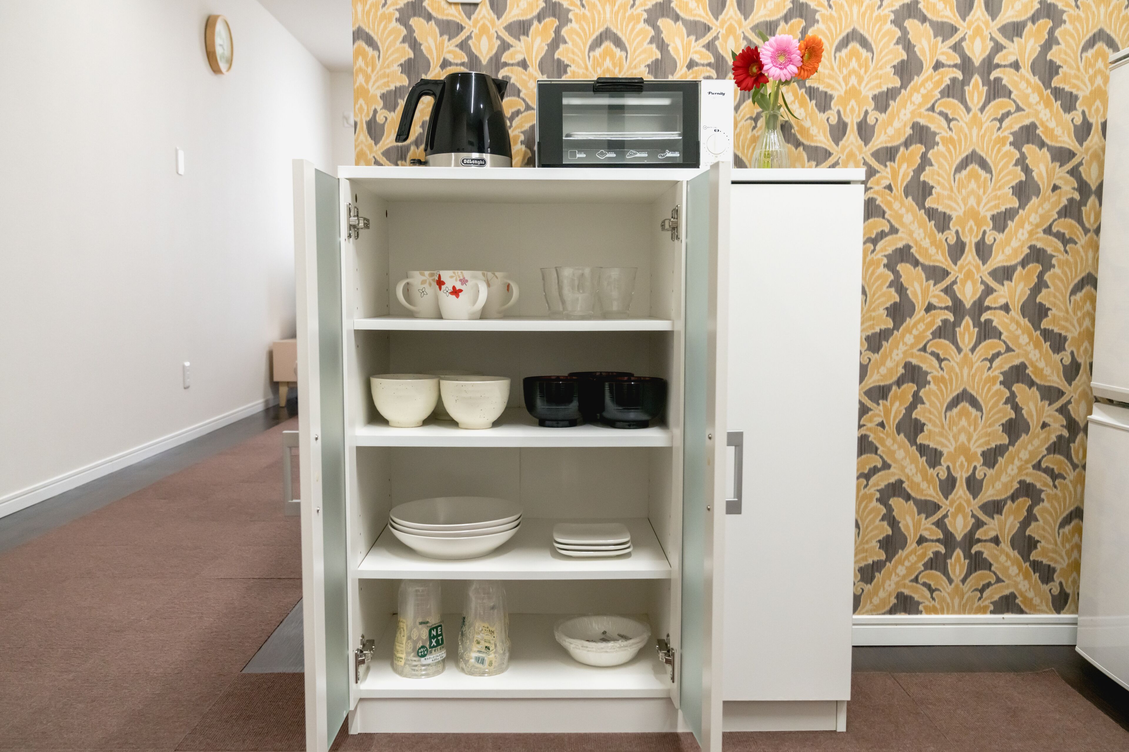 Eine Küche mit einem weißen Schrank, der verschiedene Geschirrteile, eine Kaffeemaschine und einen Toaster beherbergt.