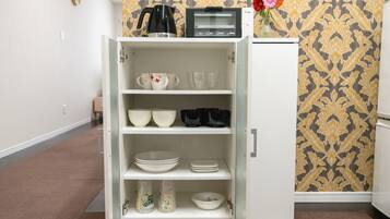 Eine Küche mit einem weißen Schrank, der verschiedene Geschirrteile, eine Kaffeemaschine und einen Toaster beherbergt.