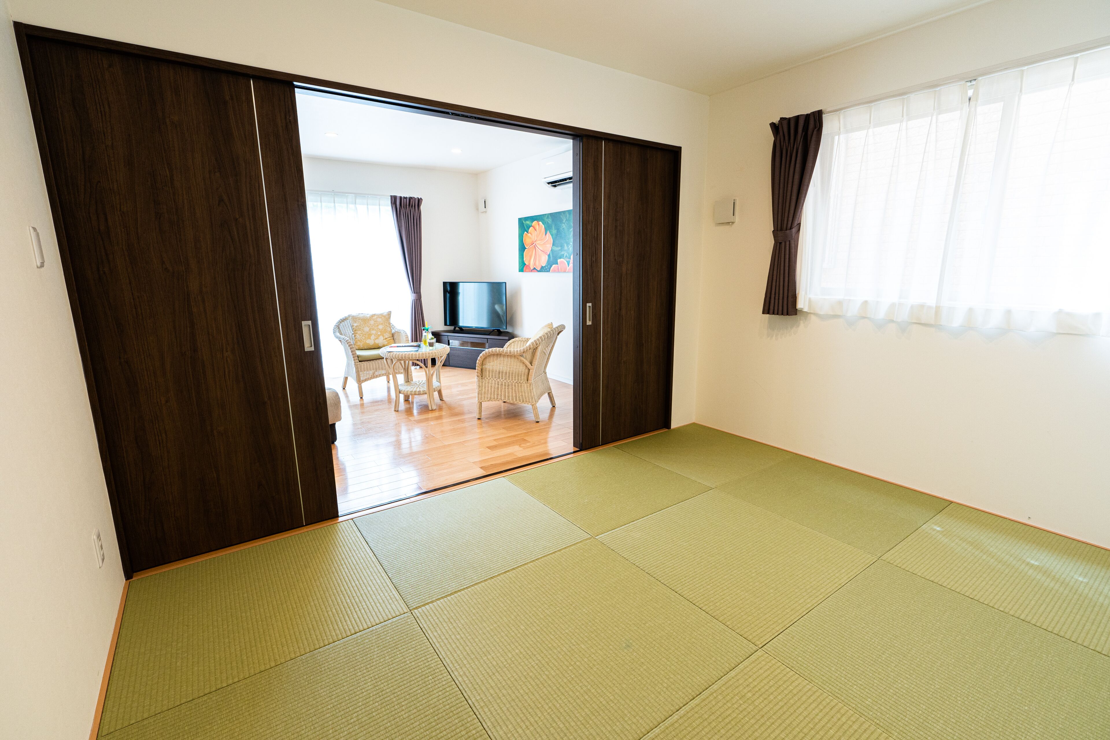 A room with tatami mats, a television, a sofa, and a painting on the wall.