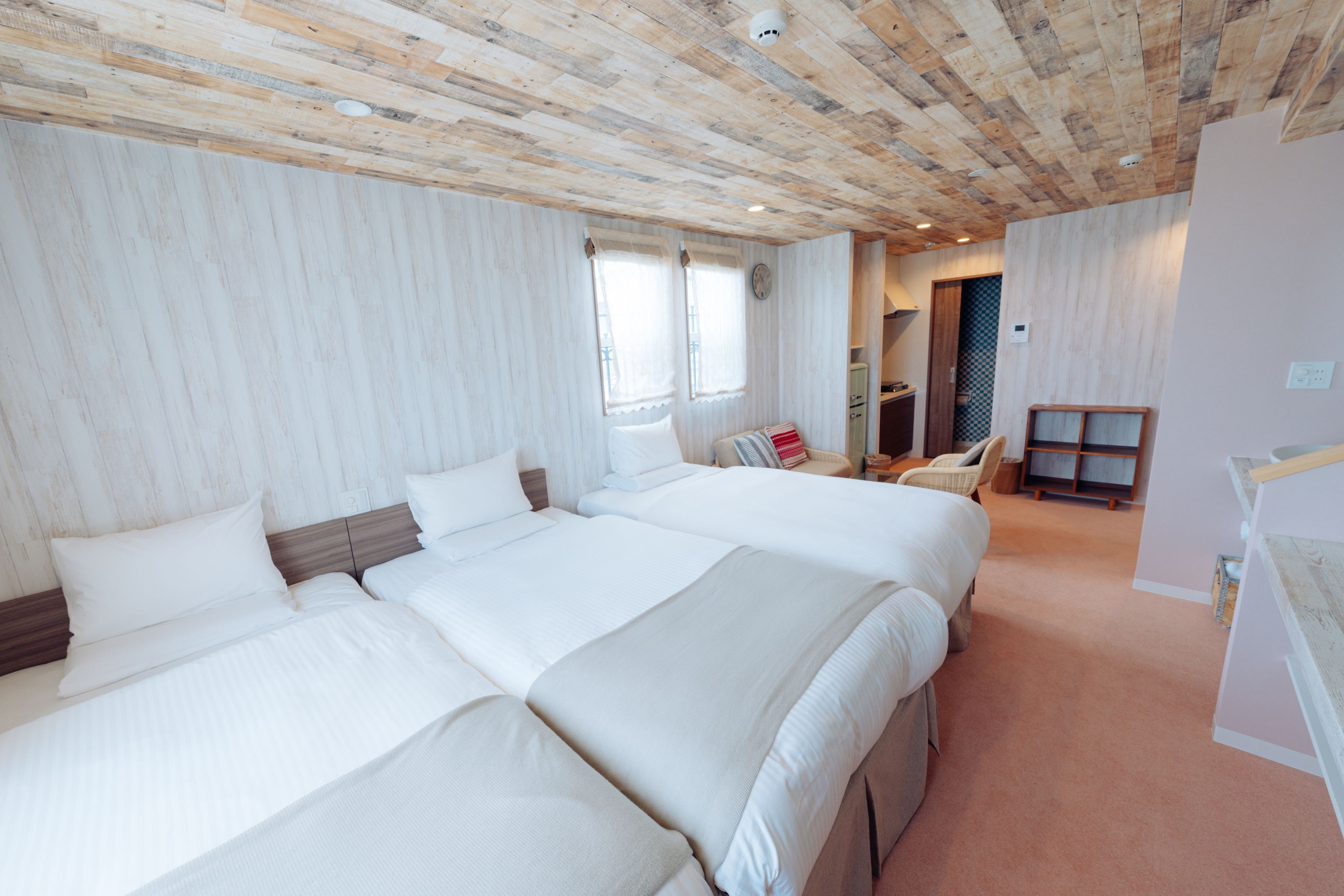 A hotel room with two beds, a wooden ceiling, a small desk, and a chair.