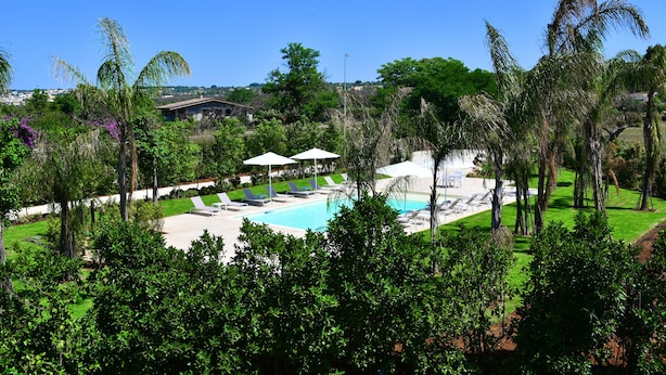 A pool area with lounge chairs and umbrellas, surrounded by palm trees and greenery. - Borgo Fiorito Relais (Parabita)