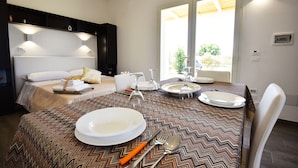 A hotel room with a dining table set for four, a bed with a headboard, and a large window providing natural light. - Borgo Fiorito Relais (Parabita)