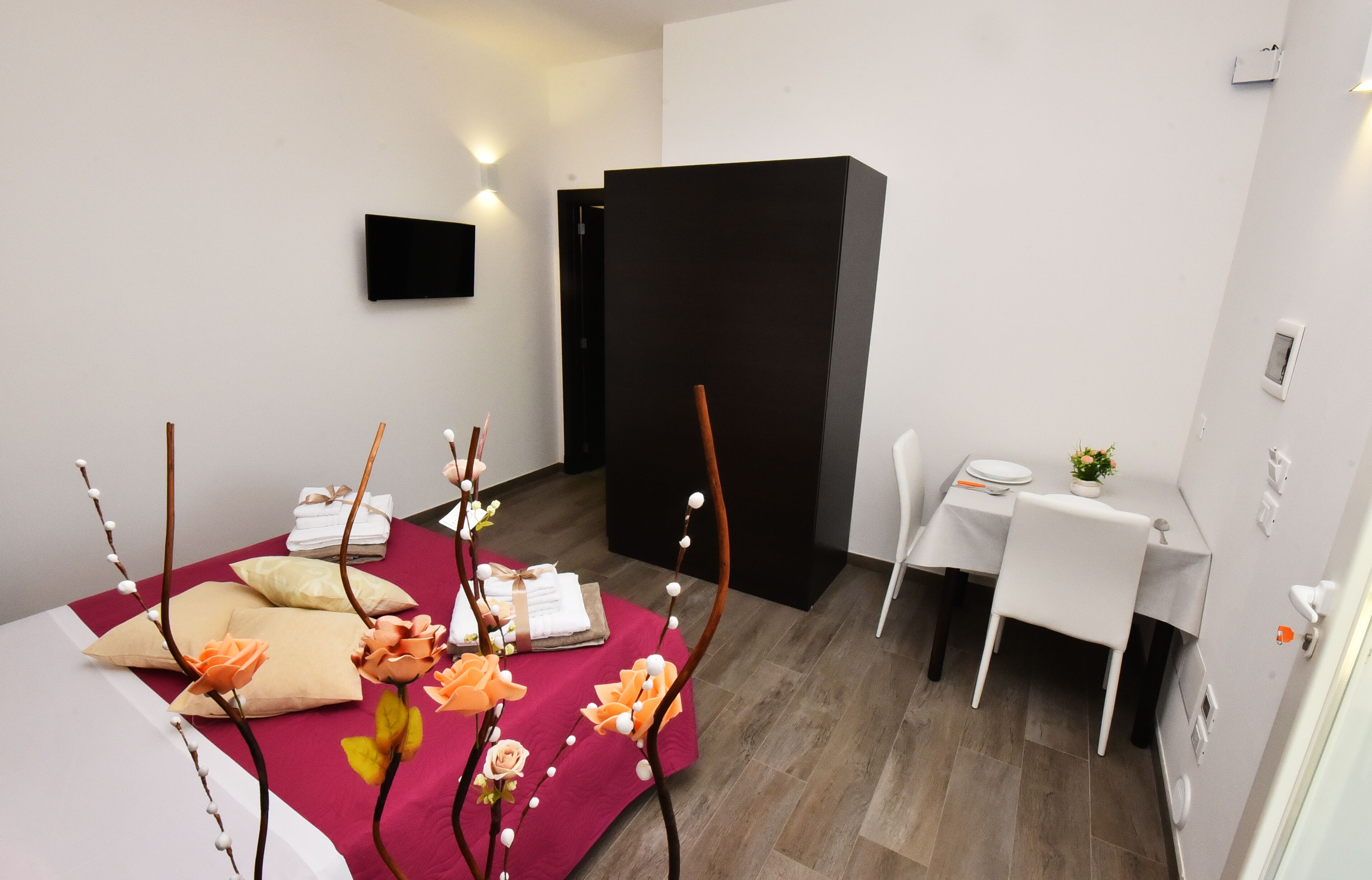 Une chambre d’hôtel moderne, équipée d’un lit, d’un bureau et d’une chaise. On y trouve des fleurs décoratives sur le lit, ainsi qu’une petite table sur laquelle est posée une plante.
