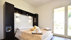 A bedroom with a bed, bedside tables, a nightstand, and a sliding glass door to a balcony. - Borgo Fiorito Relais (Parabita)