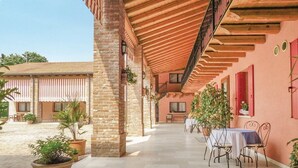 Une terrasse extérieure couverte, avec une table et des chaises, entourée de plantes en pot et d’un mur de briques.