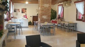 Un espace repas avec plusieurs tables et chaises, une cuisine à l’arrière-plan et une colonne en briques.