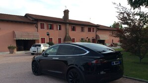 Une Tesla noire est garée devant un immeuble dont le toit est recouvert de tuiles rouges et qui possède une cheminée.