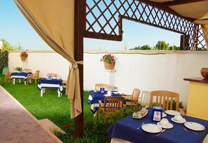 An outdoor patio with tables set for dining, covered by a canopy, and surrounded by greenery. - Terra Maris (Minervino di Lecce)