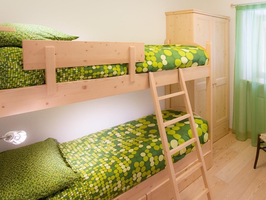 A bunk bed with a ladder, a wooden wardrobe, and a green curtain.
