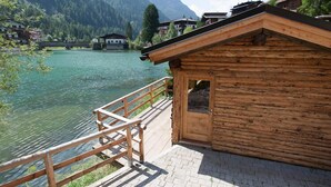 Une cabane en bois dotée d’une terrasse en bois donnant sur un lac, entourée de montagnes et d’autres bâtiments.