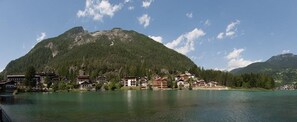 Un paese sul lago con edifici lungo la riva, una montagna sullo sfondo e cieli sereni.