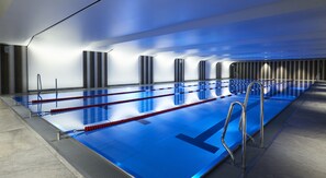 A modern indoor swimming pool with multiple lanes, clear water, and metal railings.