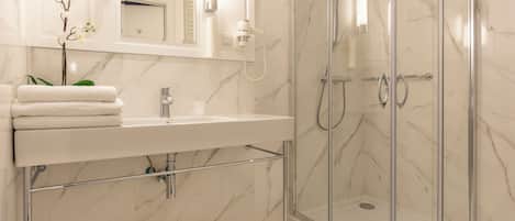 Un baño moderno con un lavabo de mármol, ducha con cerramiento de vidrio y un espejo sobre el lavabo.