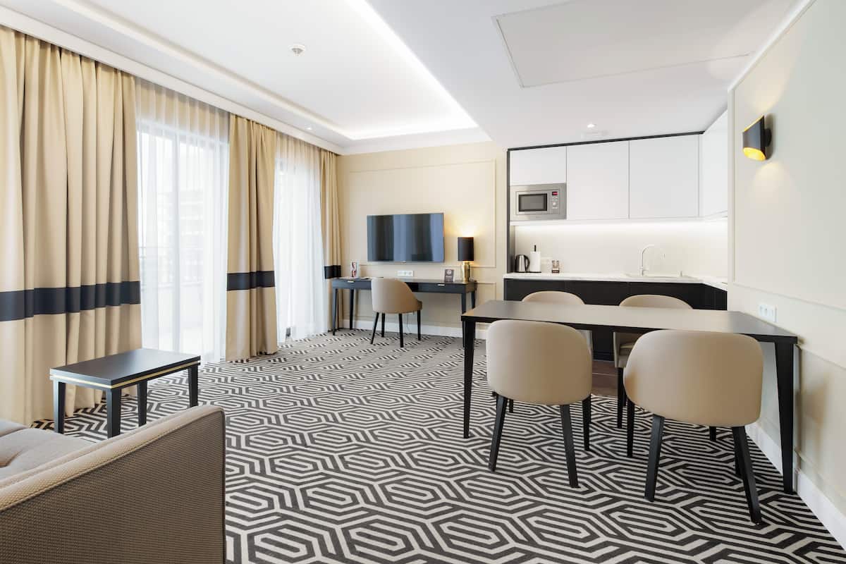 A hotel room with a geometric patterned floor, a dining area with a table and chairs, a flat-screen TV, and a microwave.