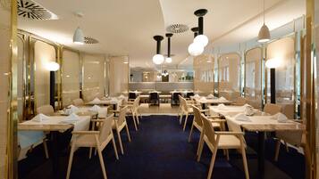Un espace de restauration moderne, doté de plusieurs tables et chaises, d’un tapis bleu foncé et d’un éclairage contemporain.