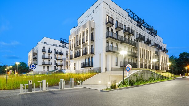Un moderno edificio residencial de varios pisos con balcones, un acceso con reja y un área ajardinada con césped.
