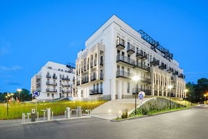 A modern multi-story residential building with balconies, a gated entrance, and a landscaped area with grass.