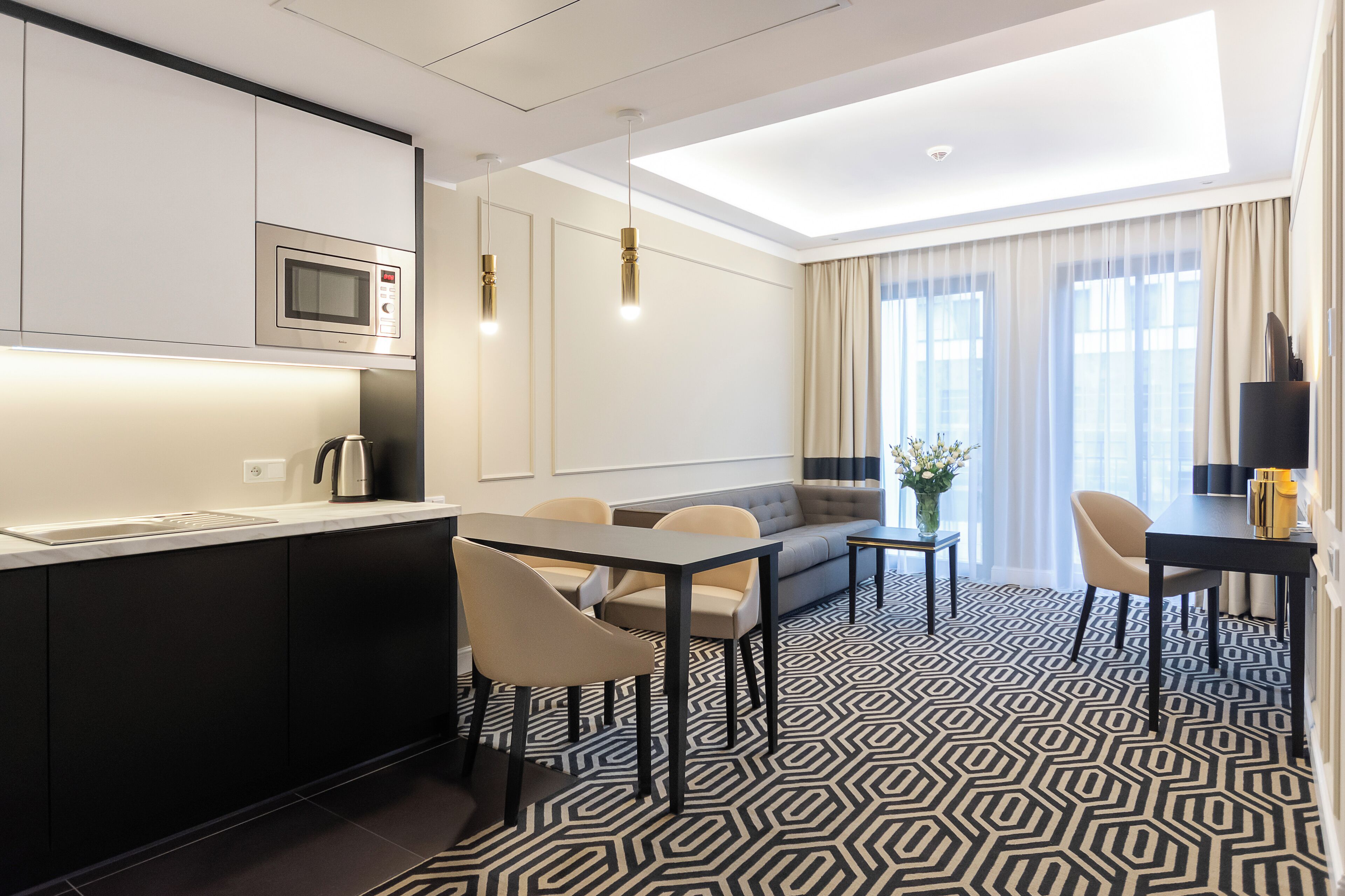 Una habitación de hotel moderna con cocina, mesa de comedor, sofá y ventanas amplias.