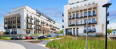 Un edificio moderno con varios balcones y un estacionamiento con coches.