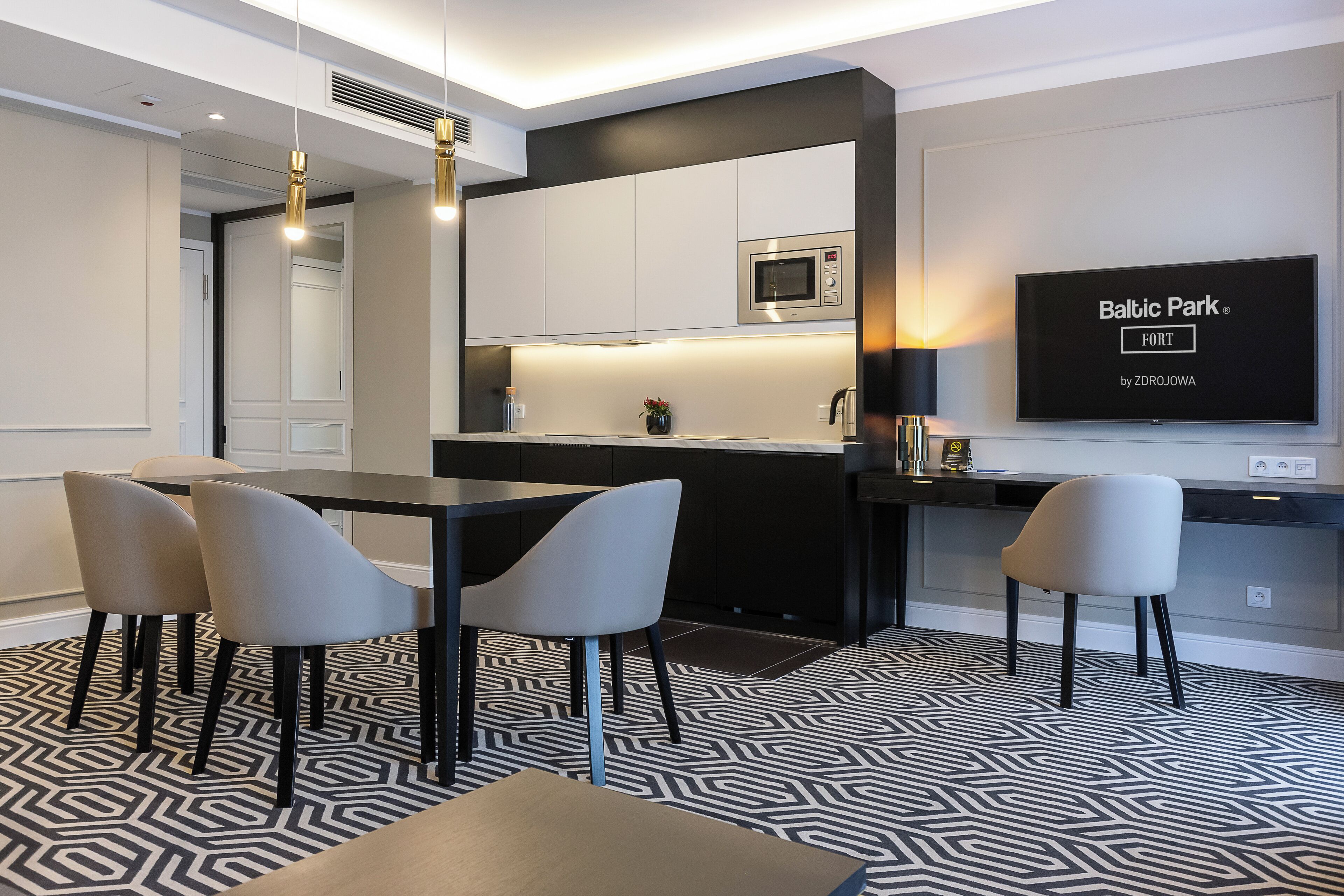 Cozinha moderna com micro-ondas, área de jantar com cadeiras e uma TV de tela plana exibindo 'Baltic Park by ZDROJOWA'.