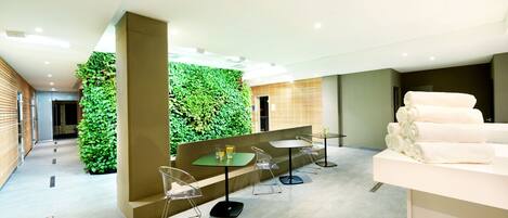 A modern indoor space with a green wall, clear chairs, a reception area with towels, and a clean, tiled floor.