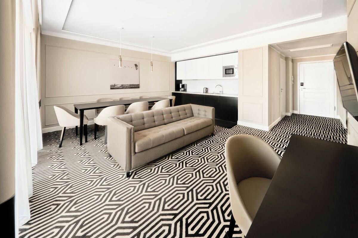 A modern hotel room with a sofa, a dining table, and a kitchen area.