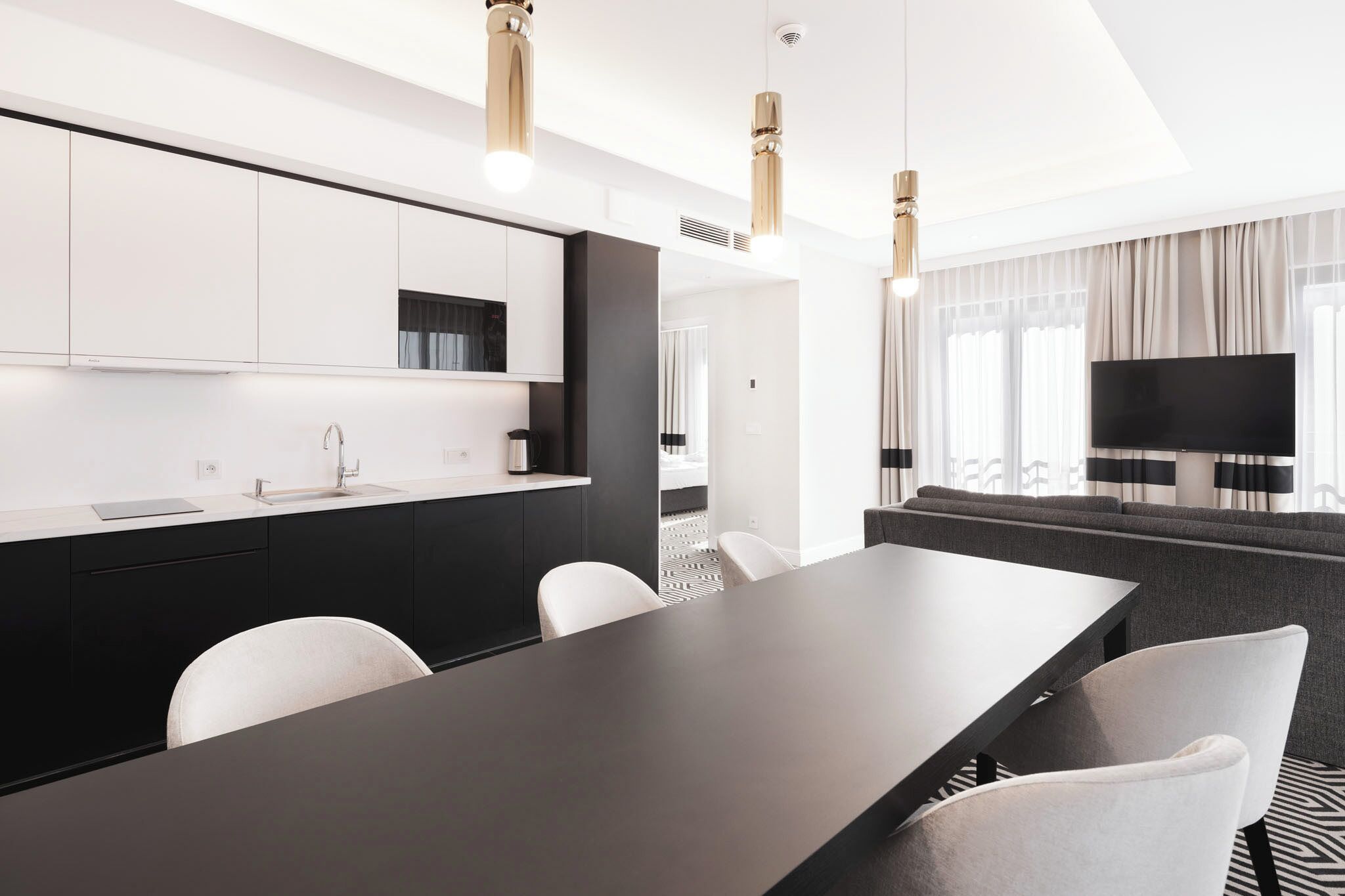 Una habitación de hotel moderna con comedor, kitchenette, televisión de pantalla plana y sofá.