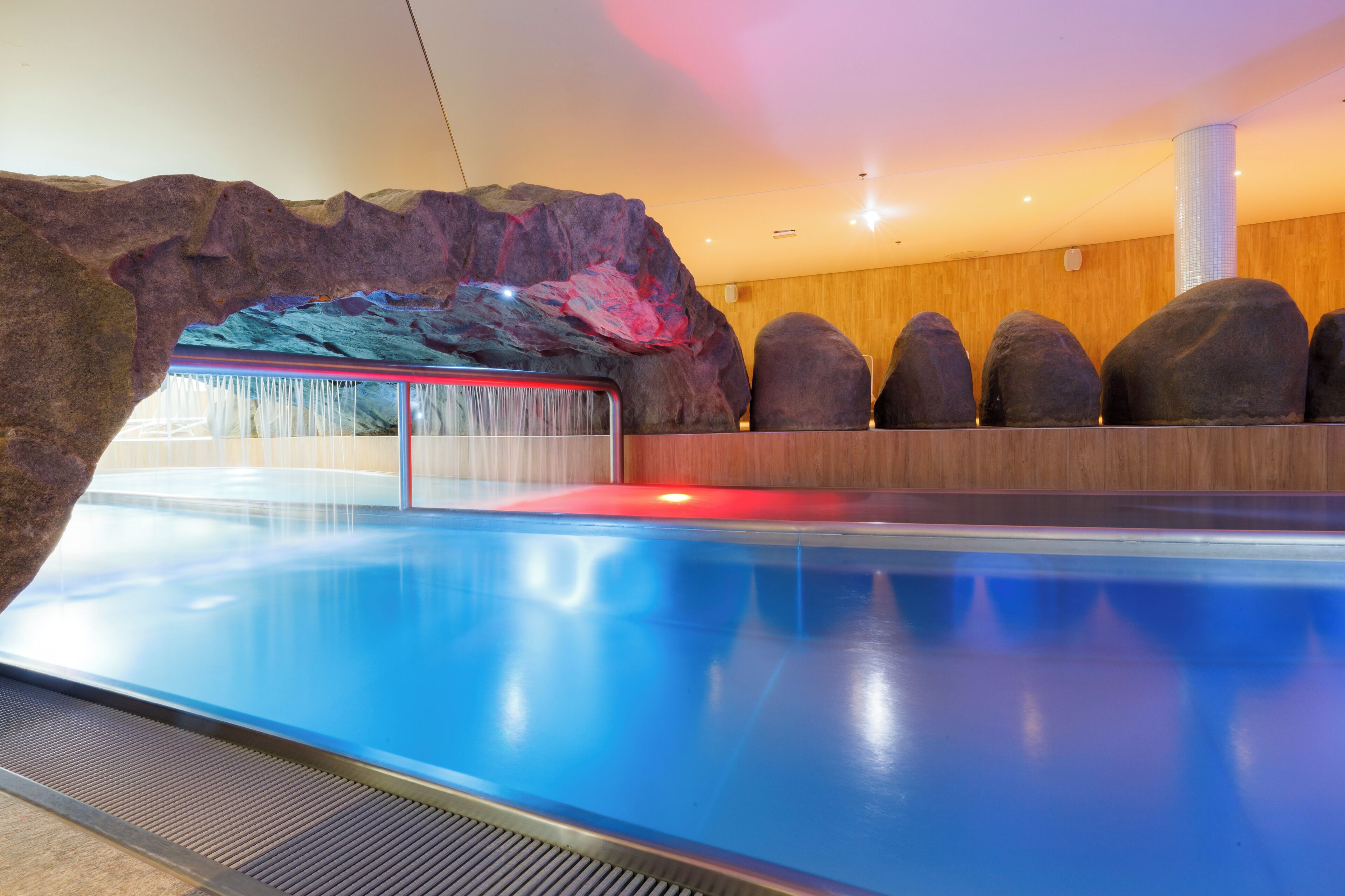 A modern indoor pool with a rock wall and a waterfall feature.