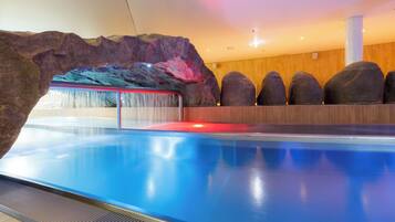 A modern indoor pool with a rock wall and a waterfall feature.