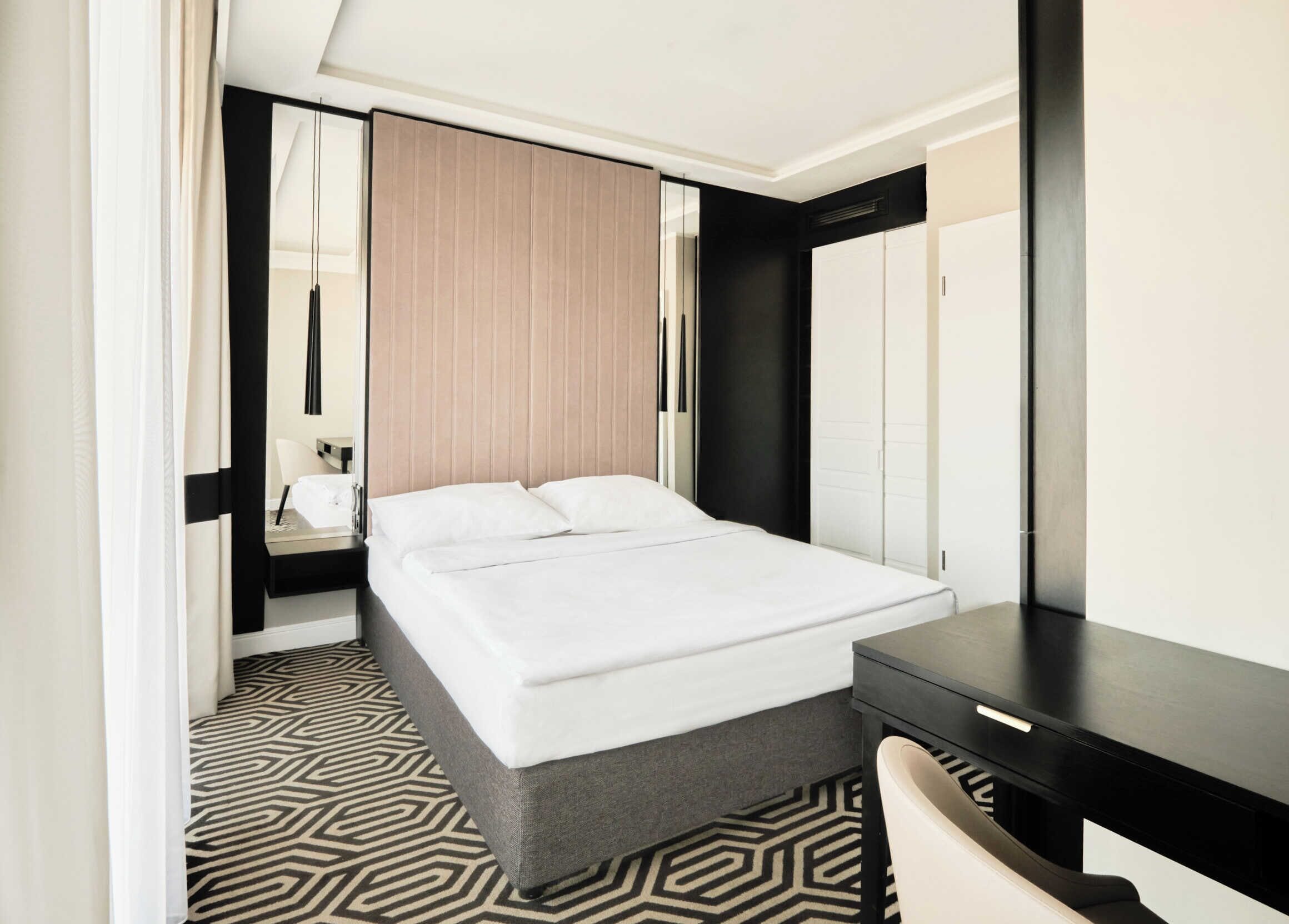A modern hotel room with a large bed, a desk, and a mirror.