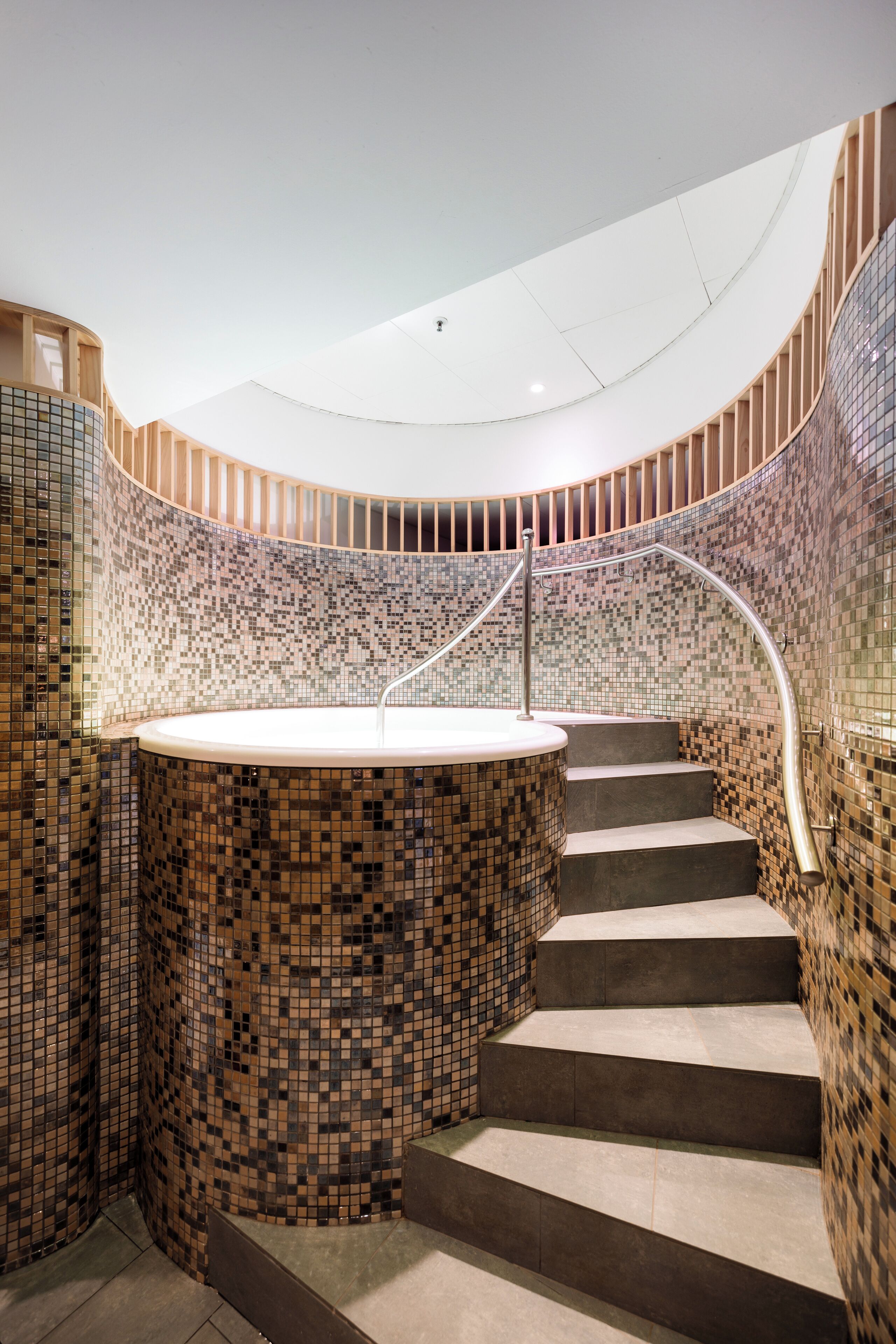 Eine Wendeltreppe mit mosaikverziertem Wandbild und einem zentralen, runden Element, möglicherweise eine Whirlpool-Badewanne oder ein Springbrunnen.
