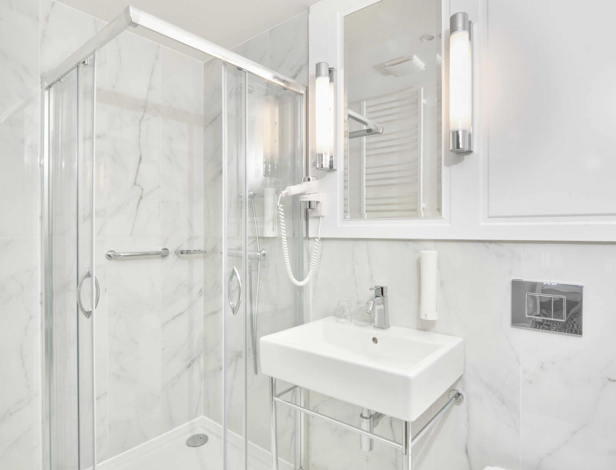 A modern bathroom with a glass-enclosed shower, a white sink, and a mirror with integrated lighting.