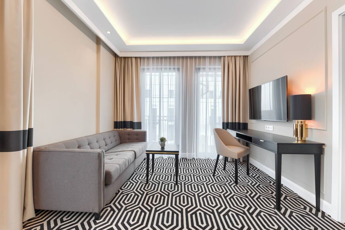 A modern hotel room with a sofa, a desk, a TV, and a patterned floor.