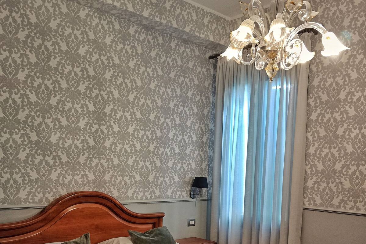 A neatly made bed with a wooden headboard, a nightstand with a lamp, and a chandelier.