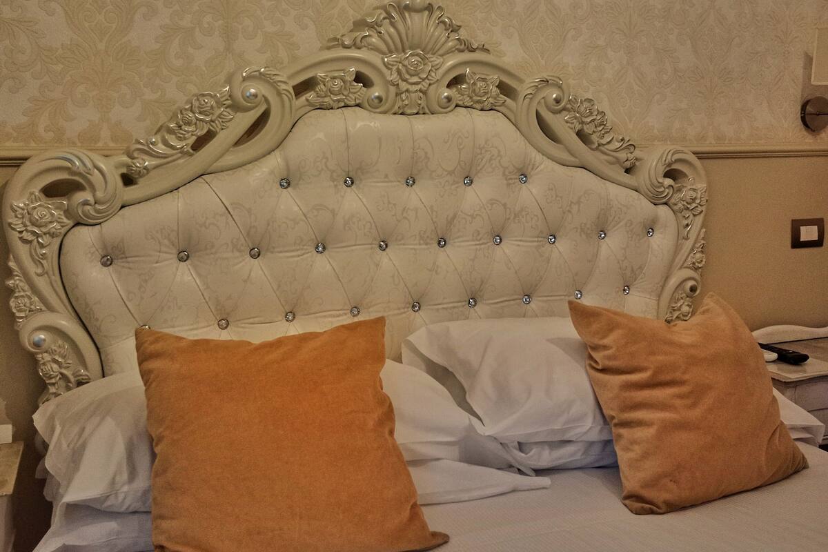 A bed with a tufted headboard, two pillows, and a nightstand with a remote control.