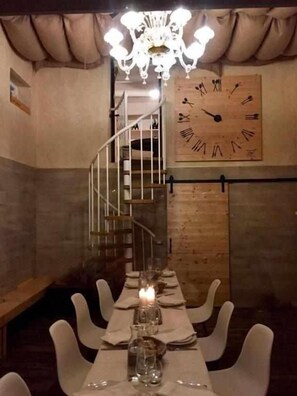A dining area with a long table, white chairs, candles, and a wooden clock on the wall. - Relais Toti B&B (Mogliano Veneto)