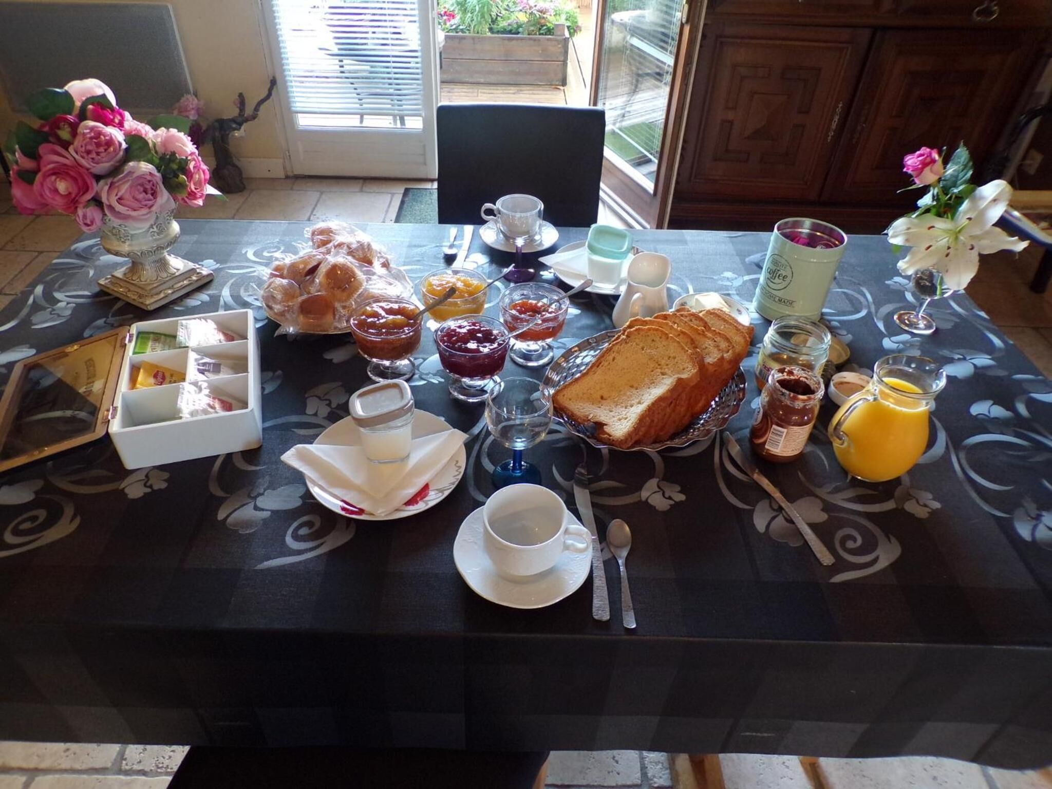 A breakfast table set with pastries, jams, bread, and beverages.