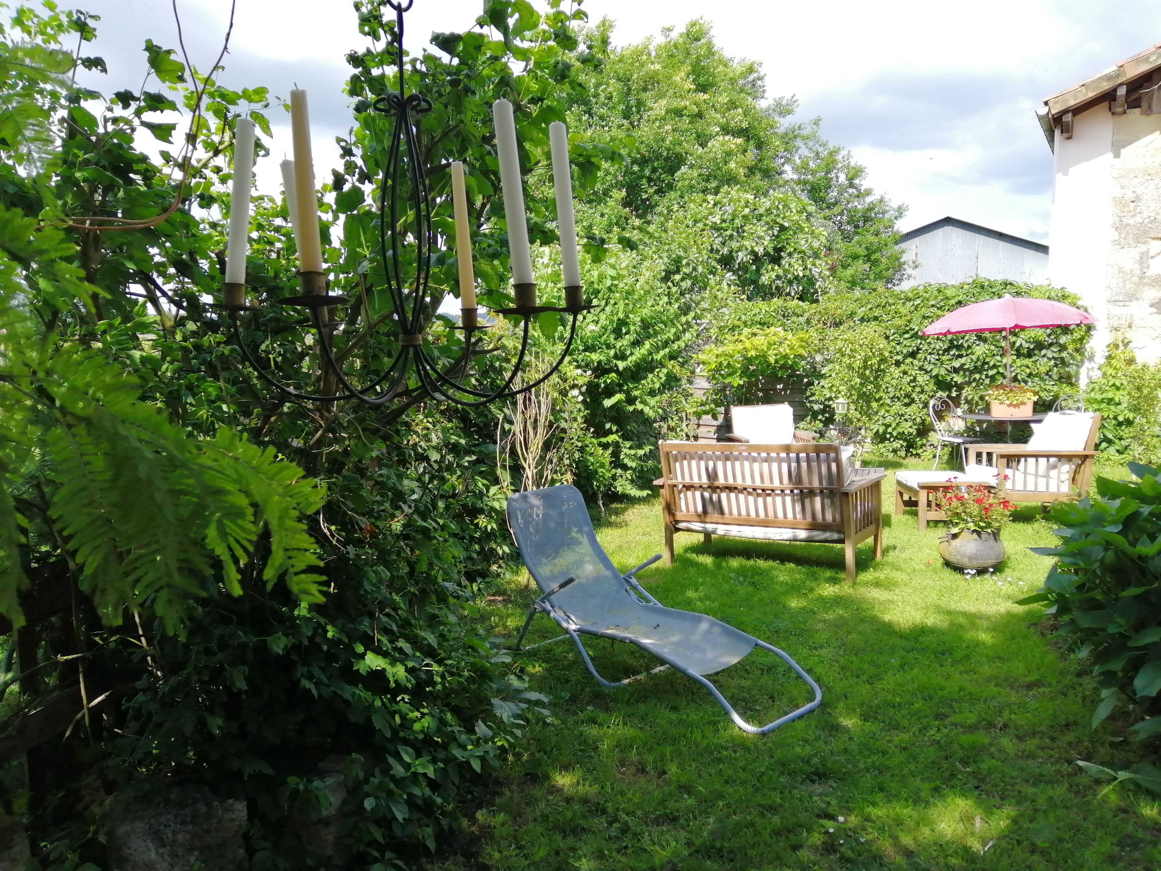 Un jardin avec un banc en bois, un fauteuil suspendu et une table surmontée d’un parasol rouge.
