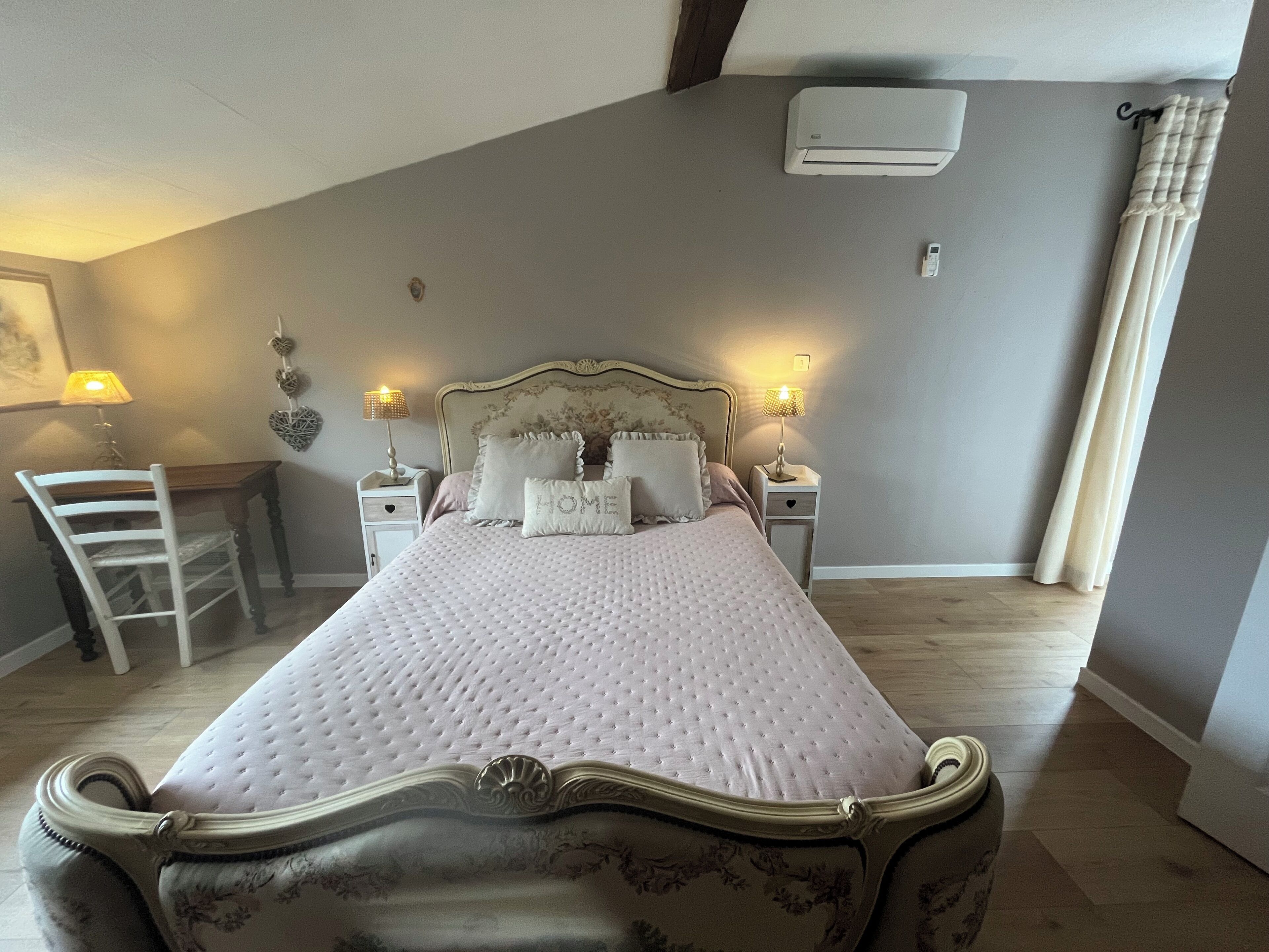 A bedroom with a bed, bedside tables, a lamp, a chair, and an air conditioning unit.