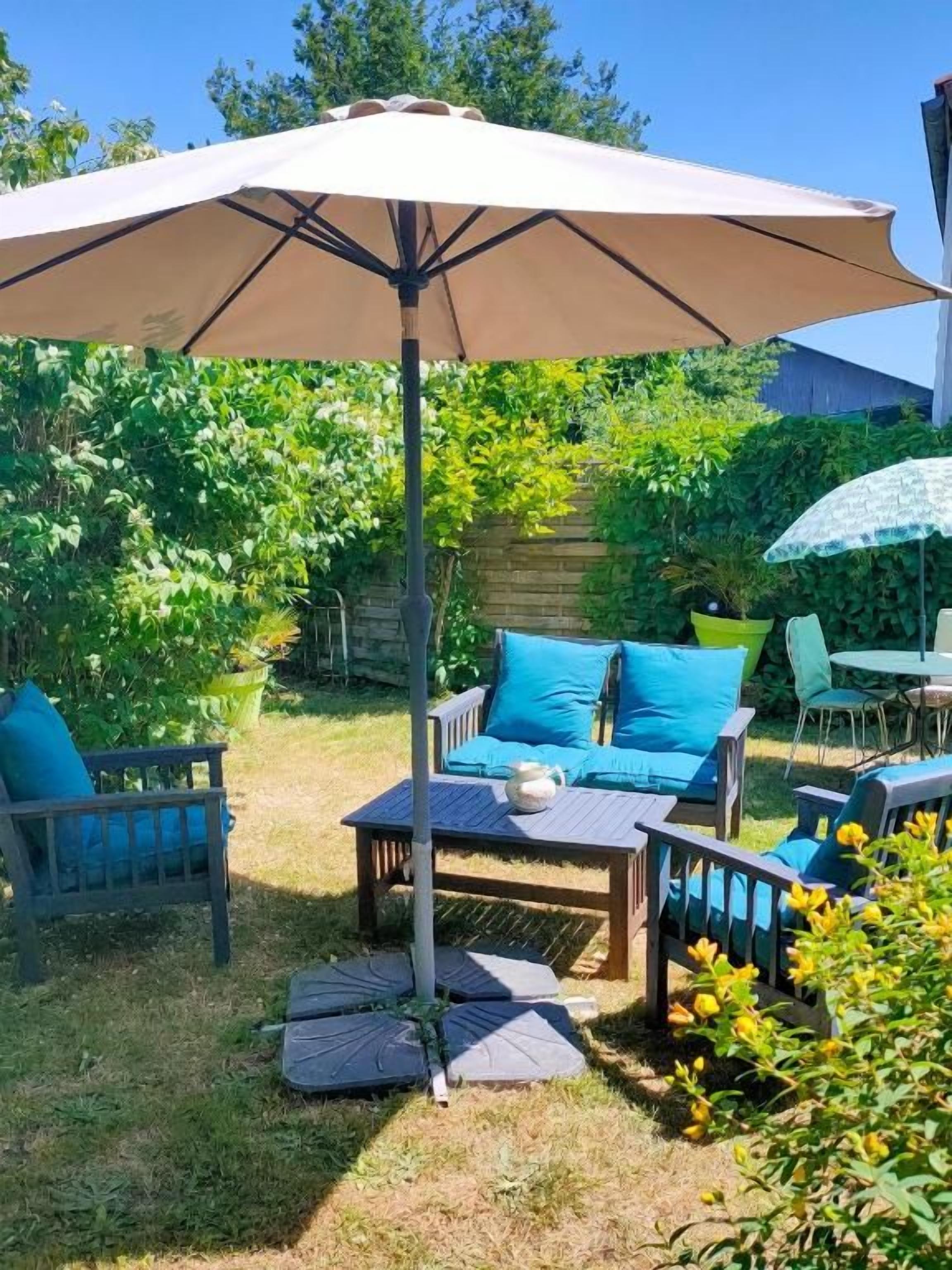 Un espace extérieur aménagé en terrasse, avec une table et des chaises, un grand parasol et un mur de pierre en arrière-plan.
