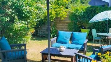 Un espace extérieur aménagé en terrasse, avec une table et des chaises, un grand parasol et un mur de pierre en arrière-plan.