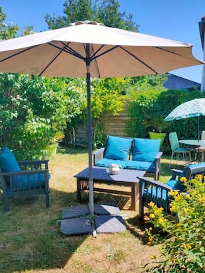 An outdoor patio area with a table and chairs, a large umbrella, and a stone wall in the background. - Chambres Peyroutas (Vignonet)