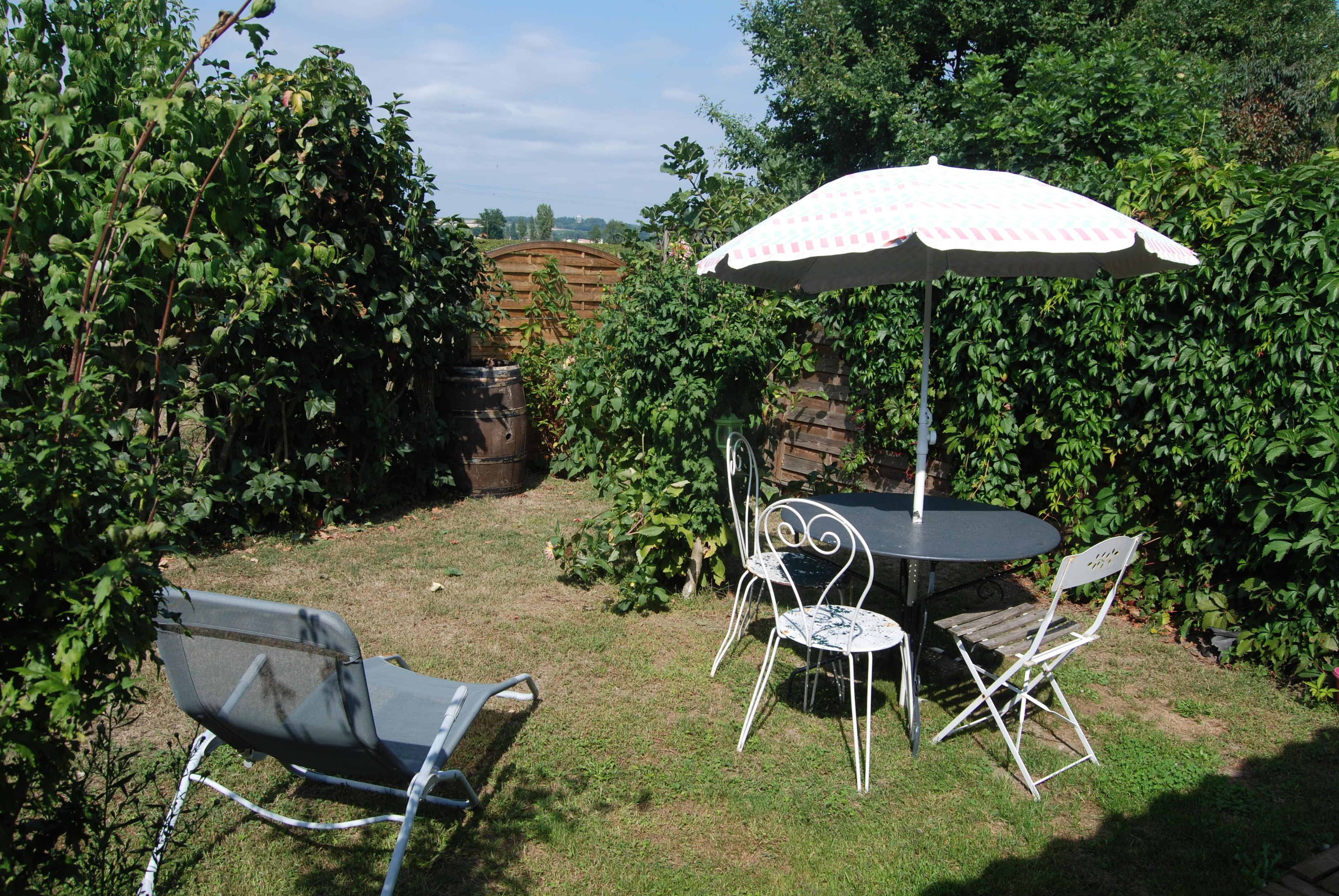 Un espace extérieur aménagé en terrasse, avec une table ronde, deux chaises et un grand parasol.