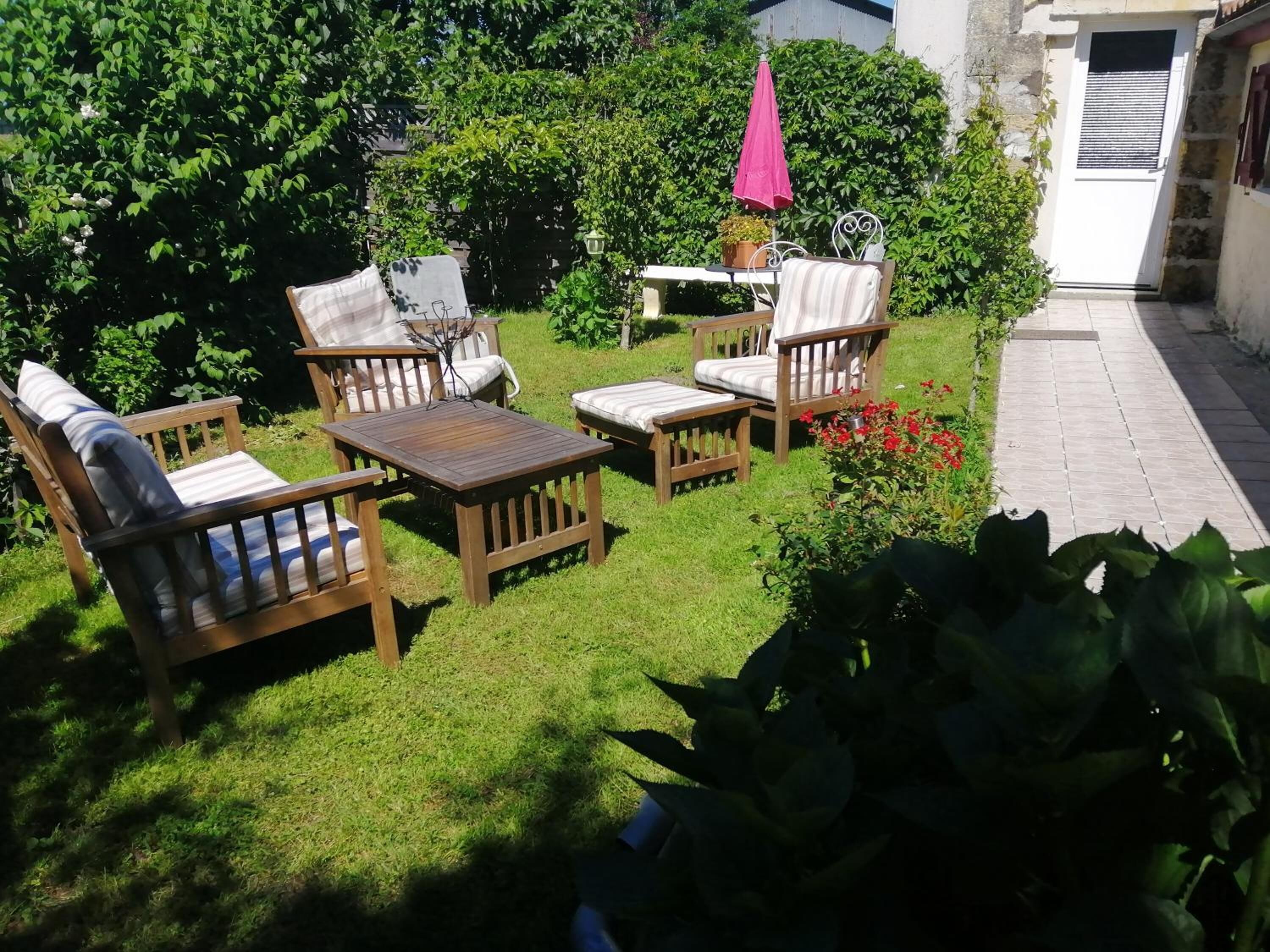 Un patio con muebles de madera y una mesa, rodeado de abundante vegetación y un pequeño jardín.