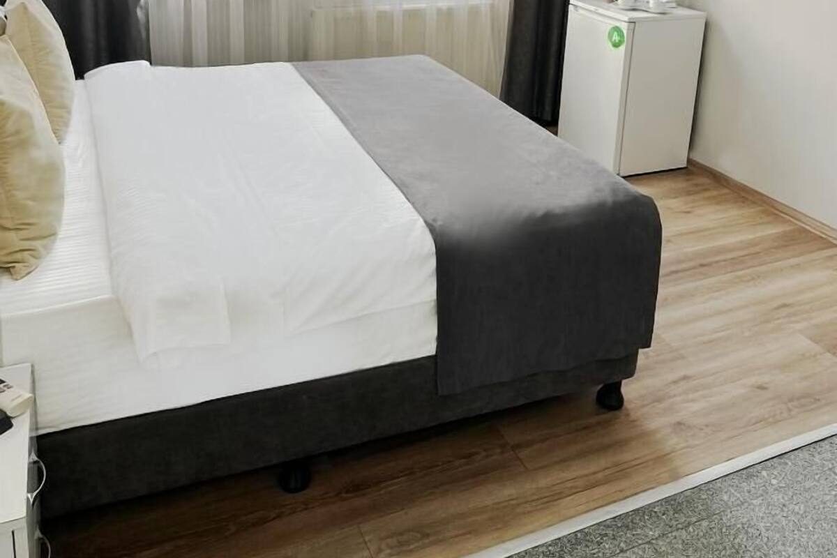 Une chambre d’hôtel avec un lit, une petite armoire blanche, une télévision et une fenêtre avec des rideaux.