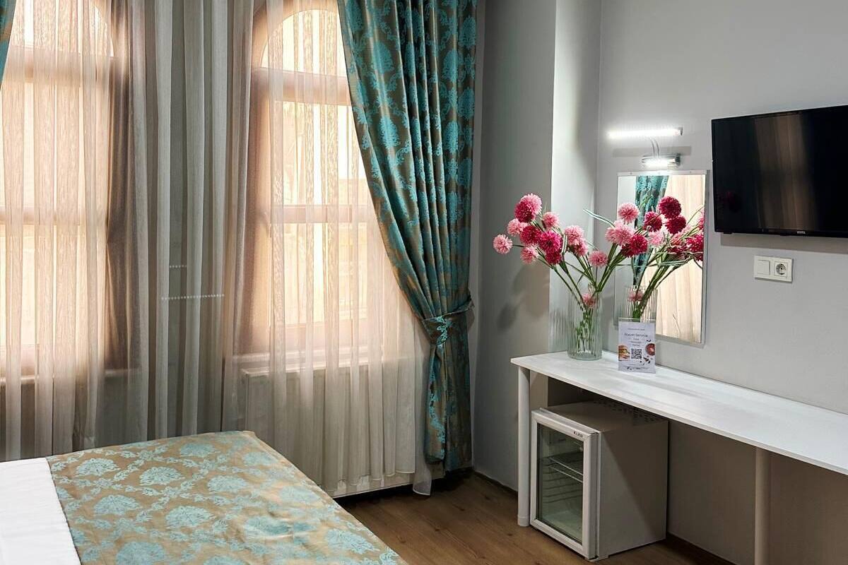 Une chambre d’hôtel avec un lit, un bureau avec une télévision et une fenêtre avec des rideaux.