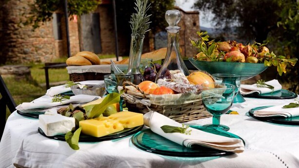 Une table dressée avec divers fromages, des fruits et du pain, le tout sur fond d’un mur de pierres rustiques.